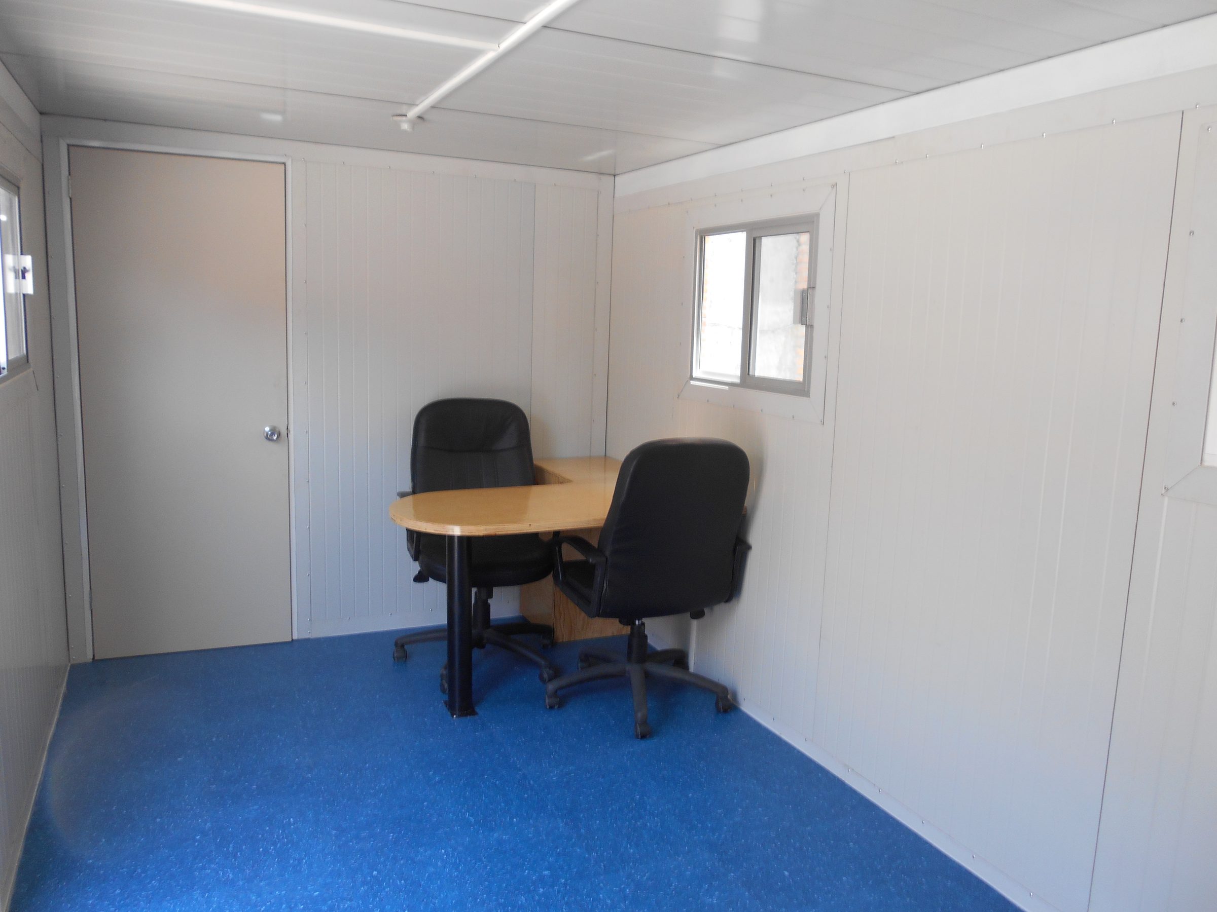 Interior de oficina móvil 8x24 con escritorio y dos sillas de director