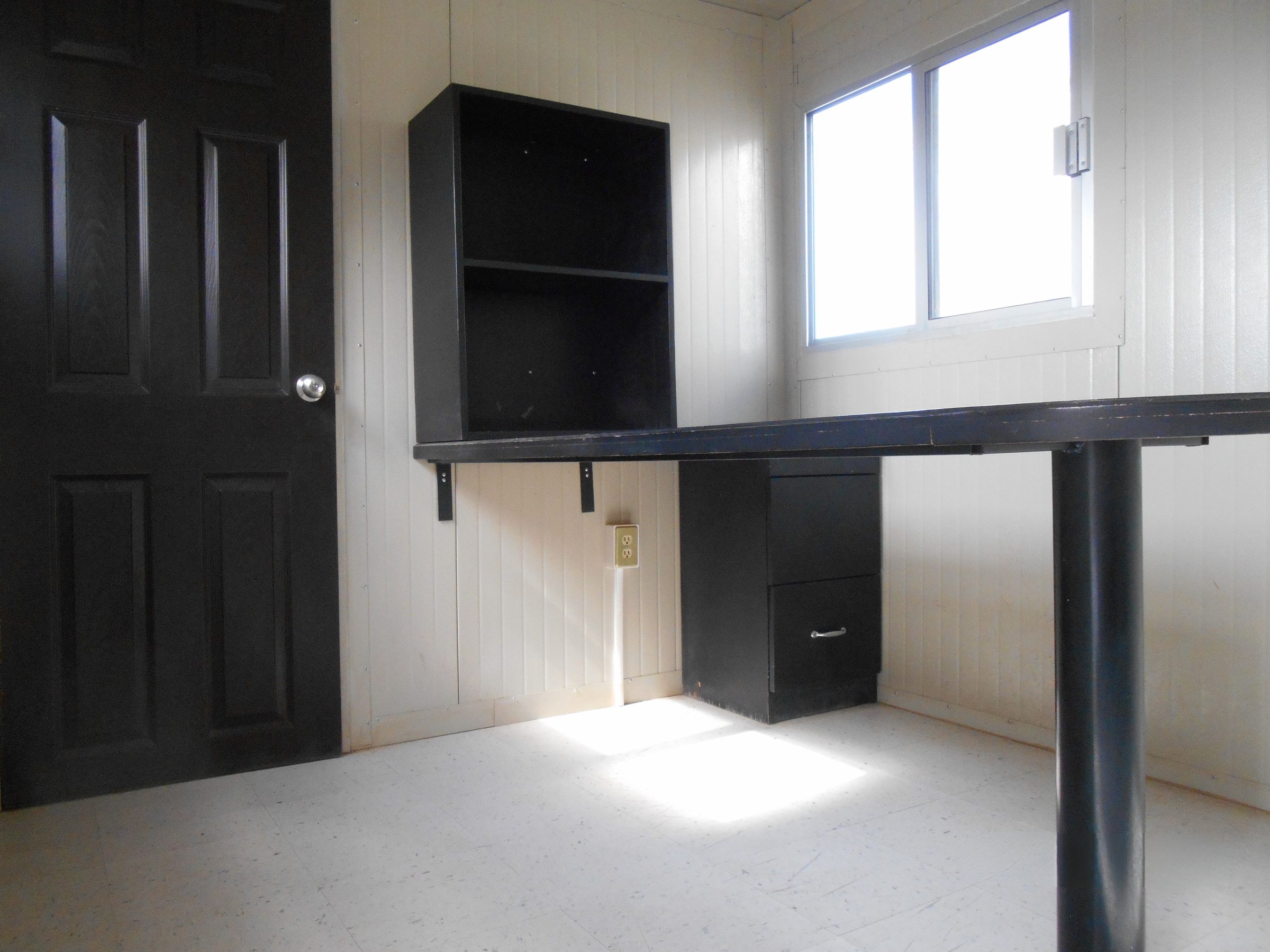 Interior de oficina móvil 8x24 con escritorio, multicontacto, ventana, puerta y doble archivero